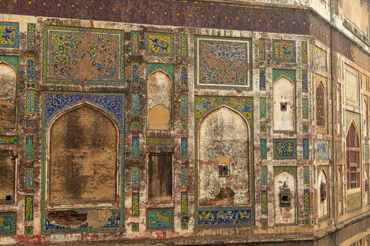 View of the aged, textured wall adorned with intricate tile work and arched niches, revealing layers of history and fading grandeur, Lahore, Punjab, Pakistan.