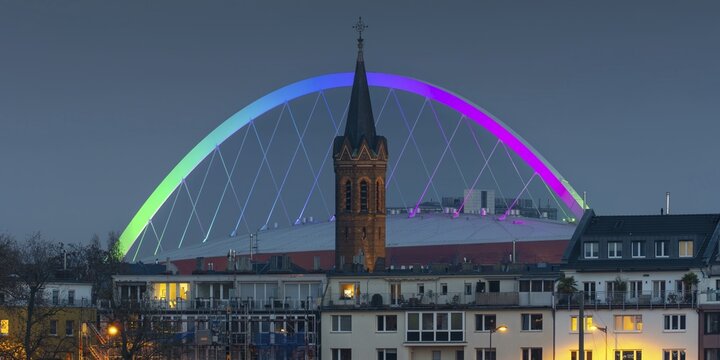 Evening view of residential buildings on the banks of the Rhine, behind them the church tower of St. John's Church and the rainbow illuminated arch of the Lanxess Arena, Cologne-Deutz, Cologne, North Rhine-Westphalia, Germany