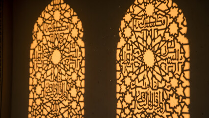 Ornate arabic calligraphy pattern projected through window grilles on wall creating warm golden light shadow play in traditional geometric style art