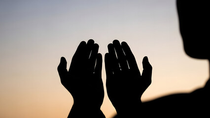 Silhouette of a person with hands raised in prayer or supplication, set against a serene sky during sunrise or sunset, evoking a sense of spirituality