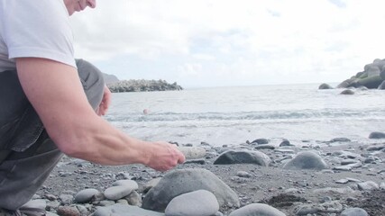 male hand carefully stacks Smooth zen-like pebbles, balanced pyramid against ocean waves, sea therapy on beach, Meditation and mindfulness, harmony, travel, and serenity coastal retreats