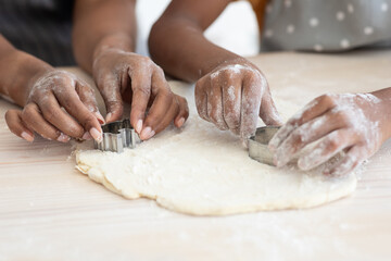Fototapeta premium Closeup of afro-american family mother and daughter hands making diverse figures with cookie cutters, black mom and kid baking together at home, using biscuit figurines, baking concept