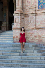 Spanish woman, with long dark hair, young and pretty, dressed in red, walking down the stairs of the Plaza de Espa&ntilde;a in Seville. Photo taken from the front.