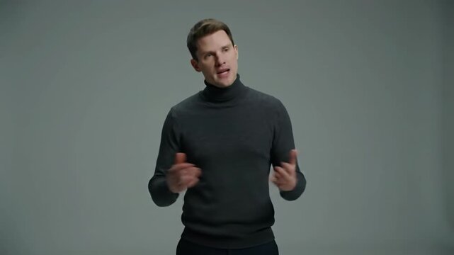 A young caucasian man in a dark grey turtleneck stands authoritatively in a minimalist studio, subtly gazing off-camera with a focused, strategic expression. Concept of strategic leadership and quiet