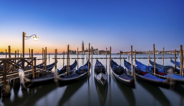 Venetian gondolas, boat dock at St Mark's Square, church of San Giorgio Maggiore in the background, long exposure at sunrise, Venice, Veneto, Italy