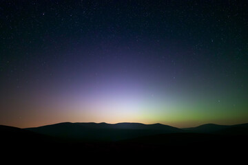 Naklejka premium Scenic night sky over mountains with glowing horizon and stars