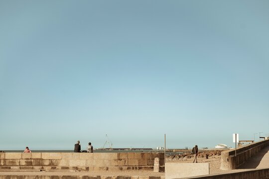 Visitors relax on a scenic stone promenade in Porto, soaking in the warm sun and gentle ocean breeze. The serene atmosphere invites peaceful reflections and light-hearted conversations