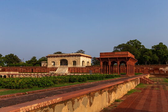 View of a serene garden with red brick pathways leading to a marble pavilion and an ornate red structure under a clear sky, Lahore, Punjab, Pakistan.