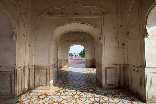 View of ornate arches framing a distant garden path under a bright sky, casting shadows on the patterned floor, Lahore, Punjab, Pakistan.