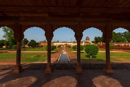 View of an ornate archway frames a vibrant garden with manicured green lawns, a central waterway, and distant architecture, Lahore, Punjab, Pakistan.