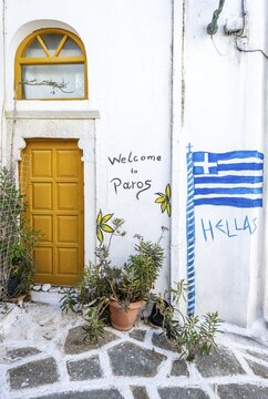 Painted house wall with inscription Welcome to Paros and Hellas with Greek flag, white Cycladic houses, picturesque alleys of the village Marpissa, Paros, Cyclades, Greece
