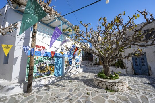 Small square with painted houses, trees and colourful flags, alleys of the village Marpissa, Paros, Cyclades, Greece