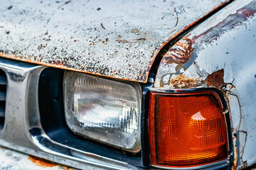 Old rusty white car with damaged paintwork on bumper and hood. Rusted ,cracked and peeling clear coat on top of vehicle bonnet hood. Car body deterioration and rust. Fragment of car hood with rust.