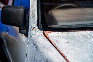 Old rusty white car with damaged paintwork on bumper and hood. Rusted ,cracked and peeling clear coat on top of vehicle bonnet hood. Car body deterioration and rust. Fragment of car hood with rust.