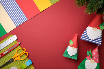 DIY paper gnomes on red background with craft tools and copy space. Festive flat lay workshop concept with cutting mat, scissors.