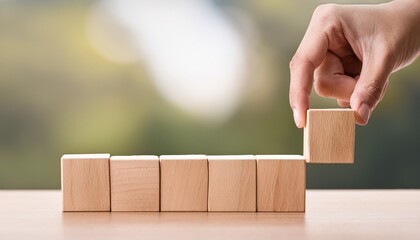 hand placing a wooden block on a row of blocks against a blurred background
