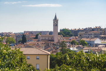 View of terracotta rooftops and sun-kissed buildings nestled around a towering church steeple against a clear sky, Pula, Istria County, Croatia.