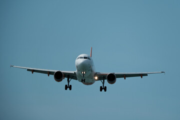 Obraz premium Passenger airplane landing head-on view against clear blue sky. Commercial jet approaching runway frontal view sunny day