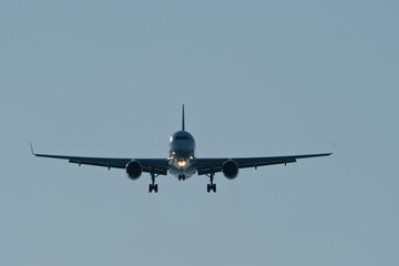 Passenger airplane landing head-on view against clear blue sky. Commercial jet approaching runway...