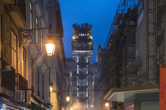 View of the illuminated Santa Justa Lift rises majestically at dusk, framed by buildings and streetlights creating an enchanting urban scene, Lisbon, Lisbon, Portugal.
