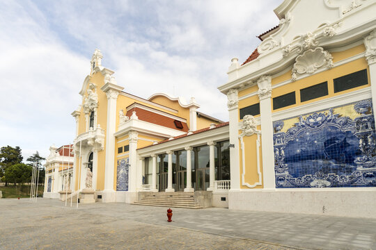 View of the Carlos Lopes Pavilion reveals intricate architectural details with yellow walls, blue tile panels, and red accents under a cloudy sky, Lisbon, Portugal.
