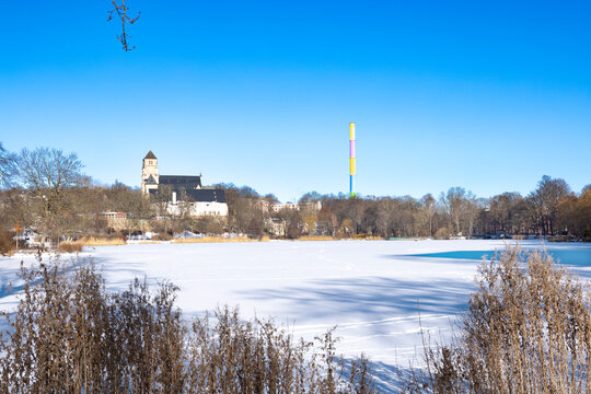 Frozen Schlossteich lake in public park with city landmarks in winter, Chemnitz Germany, snow covered ice, clear blue sky and calm urban park scenery