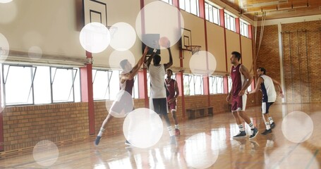 Jumping white jersey shooter holding basketball near hoop in school gym, maroon defender contesting