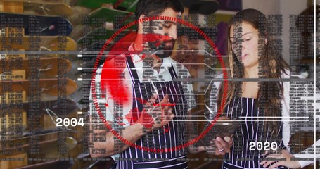 Checking bearded man and woman reviewing devices at shop, wearing striped aprons, HUD and decks