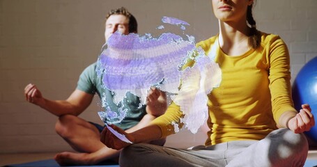Meditating woman in mustard top holding holographic world map at studio on mats with blue ball