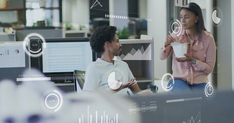 Discussing colleagues in white polo and pink blouse, sharing takeout at modern office with monitors