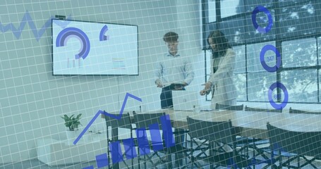 Reviewing two colleagues analyzing charts in meeting room, in blazer and white shirt, near laptop