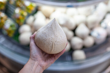 Close-up of peeled young coconut with  white husk in woman's hand. Choosing drinking coconut in supermarket in Sanya on Hainan Island, China. Sweet coconut water rich in nutrients.