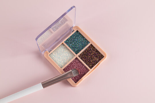 Glittery eyeshadow palette with brush on pink background