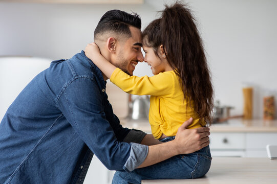 Happy Father's Day. Side View Of Cute Little Arab Girl Embracing Her Happy Dad, Smiling Middle Eastern Daddy Bonding With His Adorable Child At Home, Touching Foreheads And Smiling, Free Space