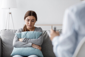 Sad european young woman suffering from depression and consults with psychologist in clinic, empty...