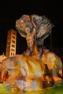 Beautiful baroque Fountain of the Tritons with medieval Basilica of Saint Mary in Cosmedin lit up at night in Rome