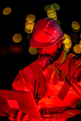 Construction supervisor giving instructions via walkie talkie at site. Night shift engineer using laptop to control building project logistics