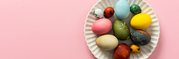 A variety of decorated Easter eggs are arranged on a circular plate against a soft pink background, showcasing vibrant colors and intricate designs for a seasonal celebration, banner