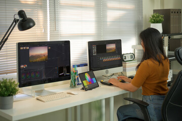 Professional female video editor editing video on his personal computer with two displays in home...