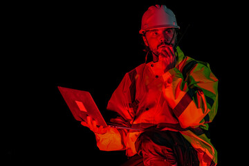 Construction supervisor giving instructions via walkie talkie at site. Night shift engineer using laptop to control building project logistics