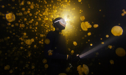 Underwater shot of the freediver swimming with the torch at night in the lake full of jellyfish.