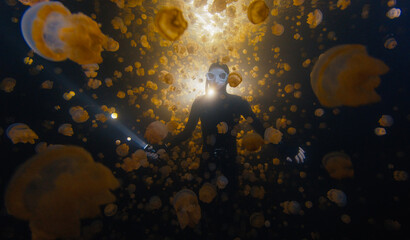 Underwater shot of the freediver swimming with the torch at night in the lake full of jellyfish.