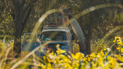 Two men unload surfing boards from the roof of the classic retro bus. Modern hippies travel by retro bus in a search of perfect waves in Brazil