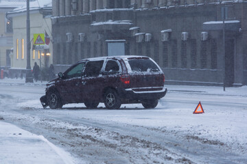 Broken SUV on snowy city street with emergency warning triangle, heavy snowfall and low visibility show winter road danger.