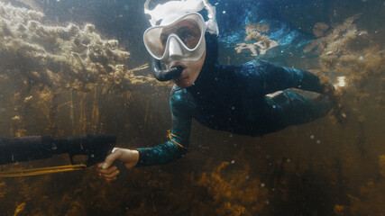 Woman with speargun swims in the lake with freshwater weed