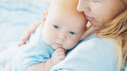 Mother caresses her newborn son with deep blue eyes in a bright room