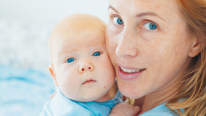 Portrait of the young mother and her newborn son with deep blue eyes in a bright room