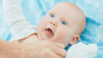 Mother plays with her newborn son with deep blue eyes in a bright room