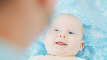 Mother plays with her newborn son with deep blue eyes in a bright room