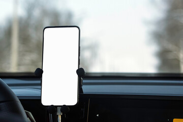 Blank smartphone screen on car dashboard mount, blurred winter road ahead, ready for navigation app mockup, UI tests, ads.